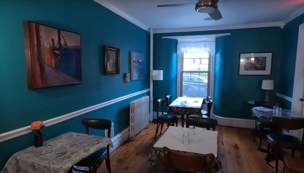 a room with tables chairs, a window, and paintings on the blue walls