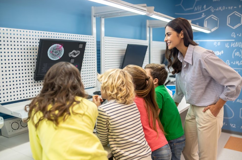 a young female teacher with children looking at a PC monitor screens during a lesson