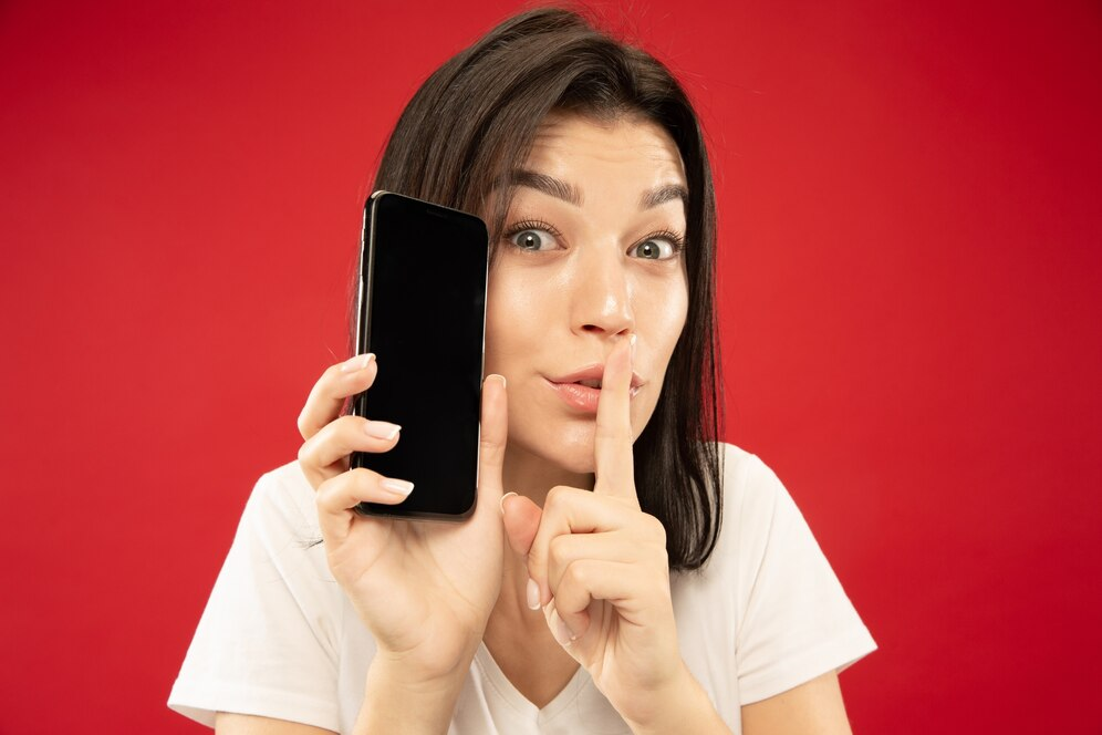 Woman gesturing silence while holding a phone